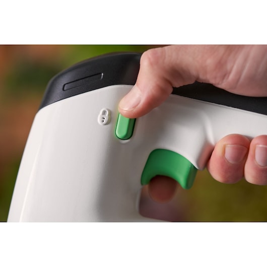 Close-up photo of a hand pressing the green power switch on a BLACK+DECKER REVJ12C white and black handle tool.