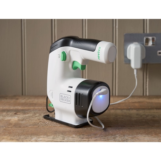 Photo of BLACK+DECKER REVJ12C handheld cordless steamer with white and black body and green buttons, charging on a wooden surface.