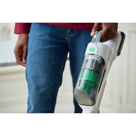 BLACKDECKER REVSV18D1 handheld vacuum with transparent dustbin and green filter, held in right hand indoors.