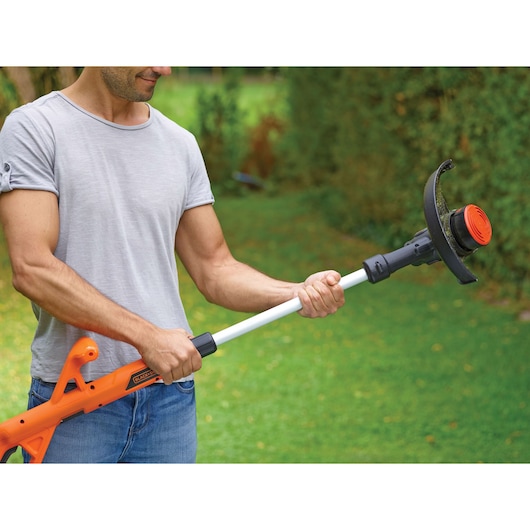BLACKDECKER ST182320 grass trimmer with orange handle, shown in use outdoors.