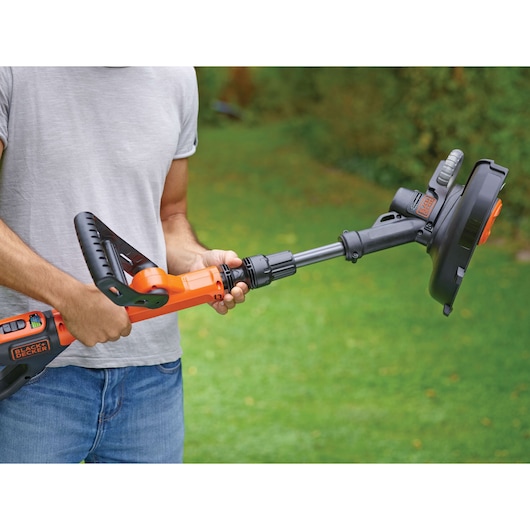 Photo of a person holding a BLACK+DECKER STC1820PCB cordless grass trimmer outside on green lawn.