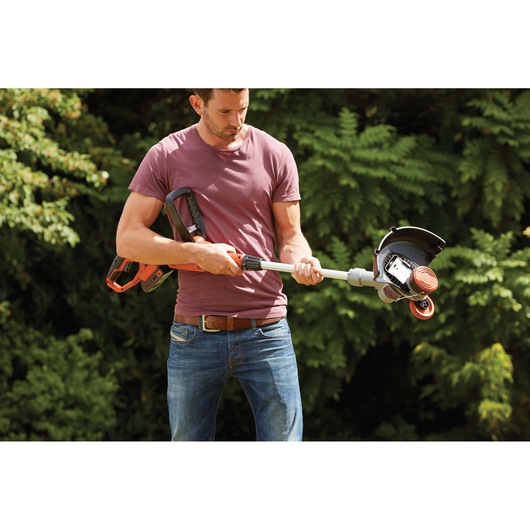 Man holding BLACKDECKER STC1820 cordless grass trimmer in garden, close-up view on trimmer and handle.
