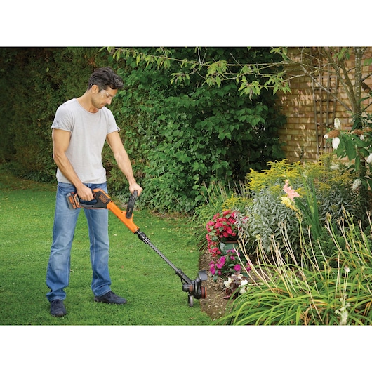 BLACKDECKER STC1840EPC grass trimmer used outdoors near flower bed.