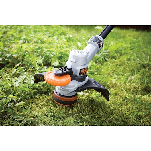 A close-up view of a BLACK+DECKER grass trimmer being used to cut grass and weeds outdoors.