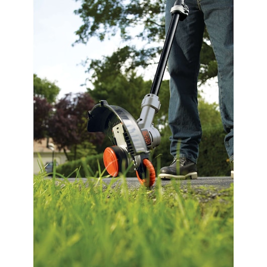 BLACKDECKER STC1840 grass trimmer in use on a lawn, close-up view showing cutting head and orange wheel.