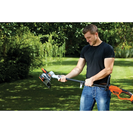 Photo of a person using a BLACKDECKER STC1840 cordless grass trimmer with orange and black handle in a garden.