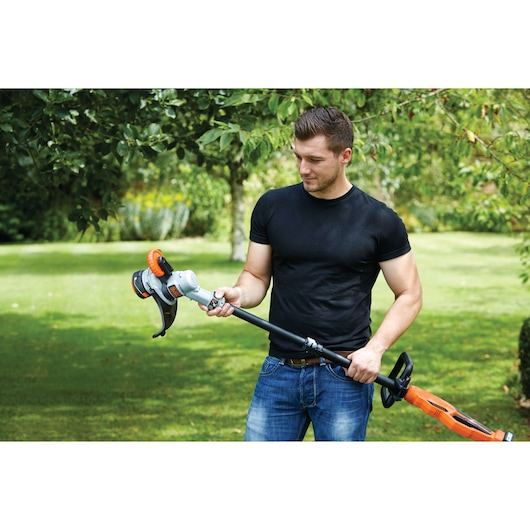 Photo of a person holding a BLACK+DECKER STC1840 cordless grass trimmer in a garden.